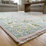 Close-up of a hand-knotted light pink Oushak rug showing intricate knots and subtle textures with natural daylight.