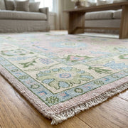 Close-up of a hand-knotted light pink Oushak rug showing intricate knots and subtle textures with natural daylight.