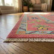 Side perspective of the Pink Hand Knotted Rug showing detailed edges and craftsmanship on a polished wooden floor in cozy indoor setting.